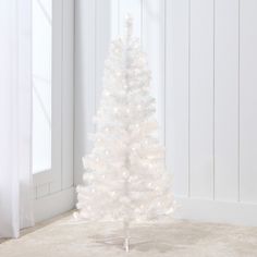 a small white christmas tree on the floor in front of a window with snow flakes