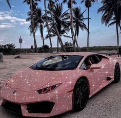 a pink sports car covered in stars and sparkles sitting on the pavement next to palm trees