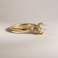 a yellow gold engagement ring with an oval cut diamond in the center and two smaller round diamonds on each side