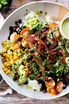 a white bowl filled with salad and dressing on top of a wooden table next to other dishes