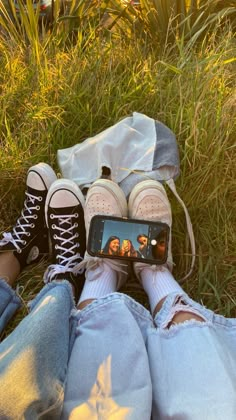 two people sitting in the grass with their feet crossed and one person holding a cell phone