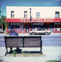 a man sitting on top of a wooden bench next to a street filled with traffic