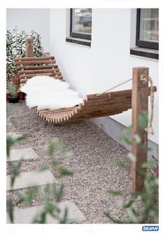 a hammock made out of wood sitting on the side of a white building