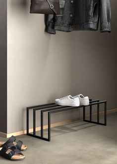 a pair of white shoes sitting on top of a black bench next to a coat rack