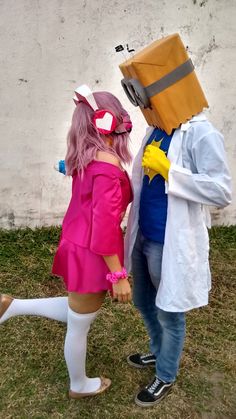 two people dressed in costumes standing next to each other on the grass and one person wearing a costume with a box on his head