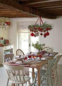 a dining room table set for christmas with ornaments hanging from the ceiling and plates on it