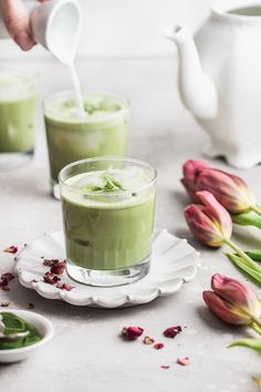 two glasses filled with green tea on top of a white plate next to tulips