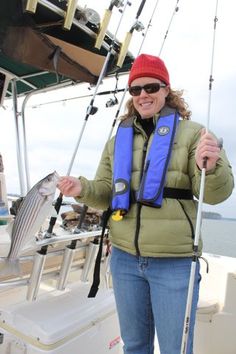 a woman standing on a boat holding a fish and fishing pole in one hand while wearing a blue life jacket