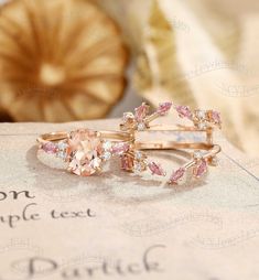 two rings with pink and white stones on them sitting on top of a piece of paper