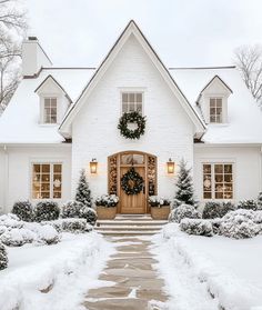 a white house covered in snow with wreaths on the front door