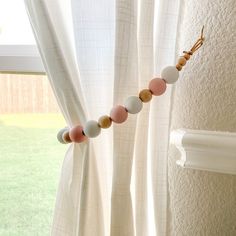 a beaded necklace hanging from the side of a curtain rod in front of a window