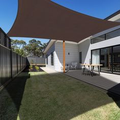 an outdoor patio with table and chairs under a brown shade sail over the back yard