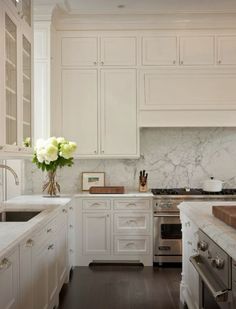 a kitchen with white cabinets and marble counter tops