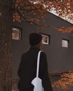 a woman in black coat and hat walking past tree with orange leaves on the ground