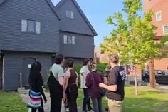 a group of people standing in front of a house on a sidewalk with one person talking to the other