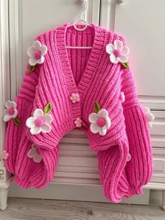 a pink sweater with flowers on it hanging from a hook in front of a door