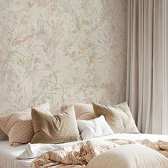 an unmade bed with pillows and blankets on it in front of a floral wallpaper