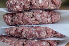 three raw hamburger patties stacked on top of each other in paper wrappers next to a wooden table