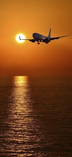 an airplane flying over the ocean at sunset