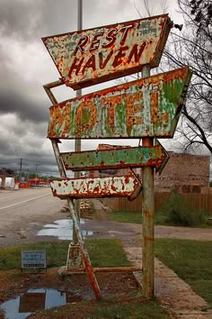 an old rusted sign sitting on the side of a road