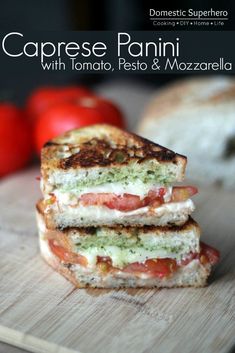 two grilled sandwiches stacked on top of each other with tomatoes in the background and text that reads caprese panini with tomato pesto & mozzarella