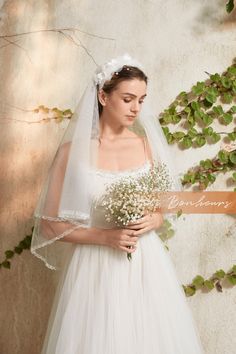 a woman in a white wedding dress holding a bouquet of flowers and wearing a veil