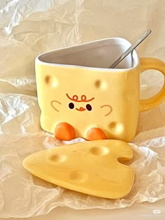 a yellow cup with a spoon in it next to a piece of cheese that is shaped like a cat