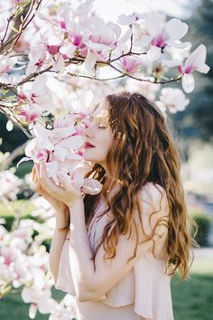 a woman standing under a tree with pink flowers on it's branches and looking up at the blossoms