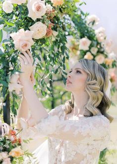 a woman in a wedding dress holding flowers up to her face while she looks at the sky