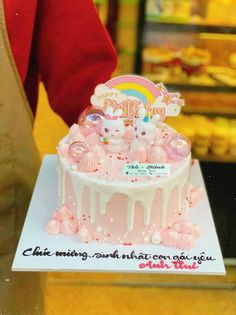 there is a pink cake with white icing on the top and rainbow decorations around it