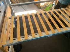 a bed frame with wooden slats on it and a person standing in the background