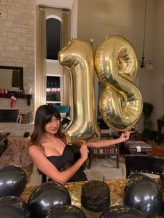 a woman holding up the number twenty five balloon in front of some black and gold balloons