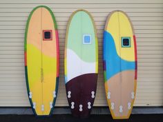 three surfboards are lined up against a garage door, one is painted multicolored