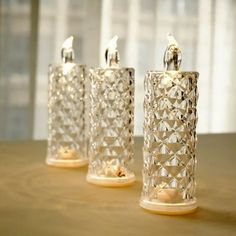 three glass candlesticks sitting on top of a wooden table next to a window