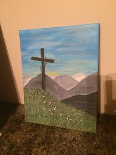 a painting of a cross on top of a hill with mountains in the back ground