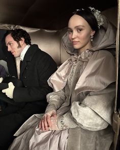 a man and woman dressed in period clothing sitting on a train together, looking at the camera