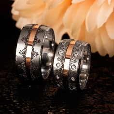 two wedding bands with intricate designs on them next to a white and pink flower in front of a black background