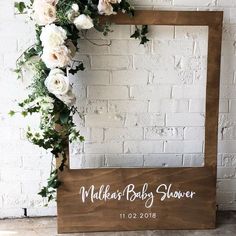 a wooden frame with white flowers and greenery on the side, next to a brick wall