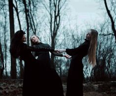 two women in long black dresses holding hands with each other while standing in the woods