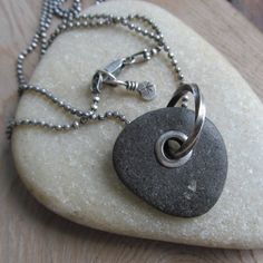 "Mens Riveted Beach Stone Necklace Silver Beach Stone Charm: This is a substantial pendant made from a natural black beach stone with a big 'ol sterling silver tube rivet and heavy silver ring. The stone has a nice soft feel and rugged texture. It hangs from a weighty sterling diamond-cut ball chain that is approximately 23.5 inches long and has a sturdy lobster-claw clasp. Pendant measures 1 1/4 inch high including ring by about 1\" wide. I had this in mind for a man, but a woman can pull this Boho Charm Bracelet, Artsy Accessories, Beach Business, Brown Tourmaline, Beach Stones Jewelry, Pebble Jewelry, Metal Stamped Jewelry, Black Beach, Long Silver Necklace