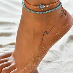 a woman's foot with two bracelets on it, and the ankle is covered in sand