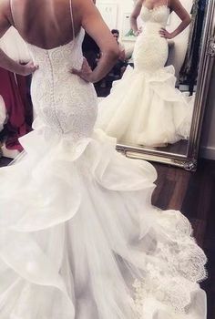 a woman standing in front of a mirror wearing a wedding dress with ruffles