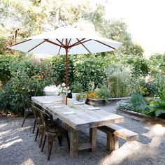 an outdoor dining table and umbrella in the middle of a graveled area with potted plants