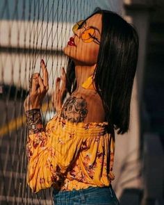 a woman with tattoos on her face standing behind a wire fence and looking up at the sky