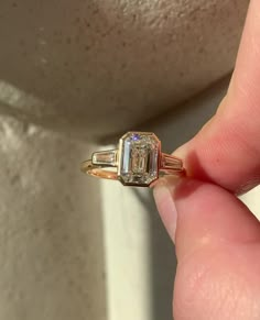 a woman's hand holding an engagement ring with two baguettes on it