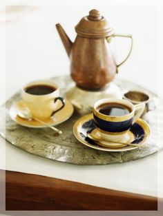 two cups of coffee sit on a tray next to a teapot and saucer