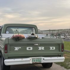 an old ford pick up truck is parked on the side of the road in front of a dock