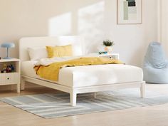 a white bed with yellow sheets and pillows in a room next to a blue chair