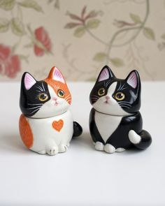 two small black and white cats sitting next to each other on a table with flowers in the background