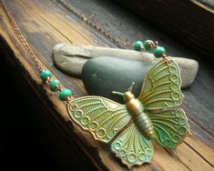 a green butterfly necklace sitting on top of a wooden table next to a rock and some beads